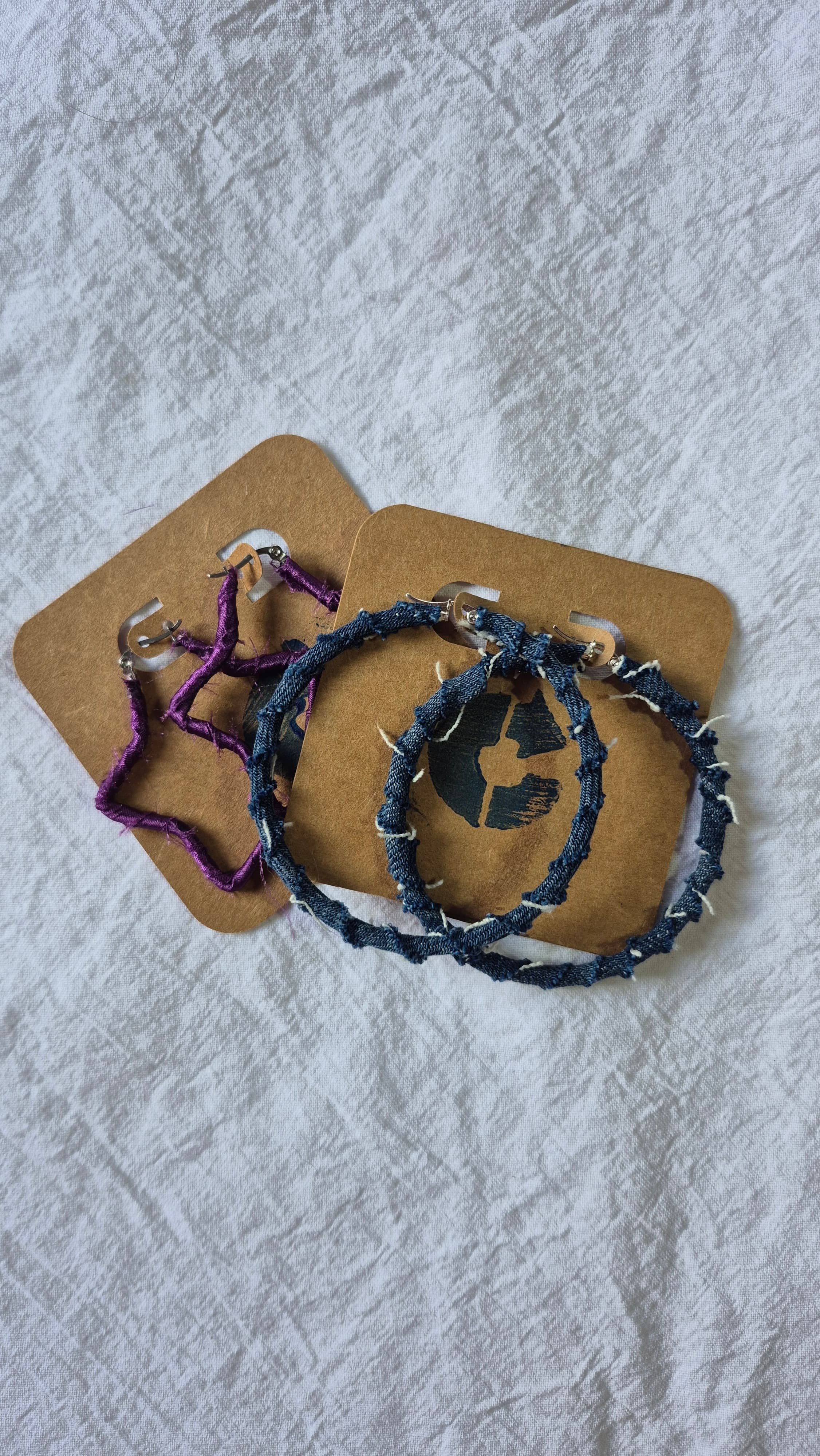 Dos pares de aros de CÍCLICA en sus tarjetas: una estrella violeta y unas argollas de denim con puntadas a la vista