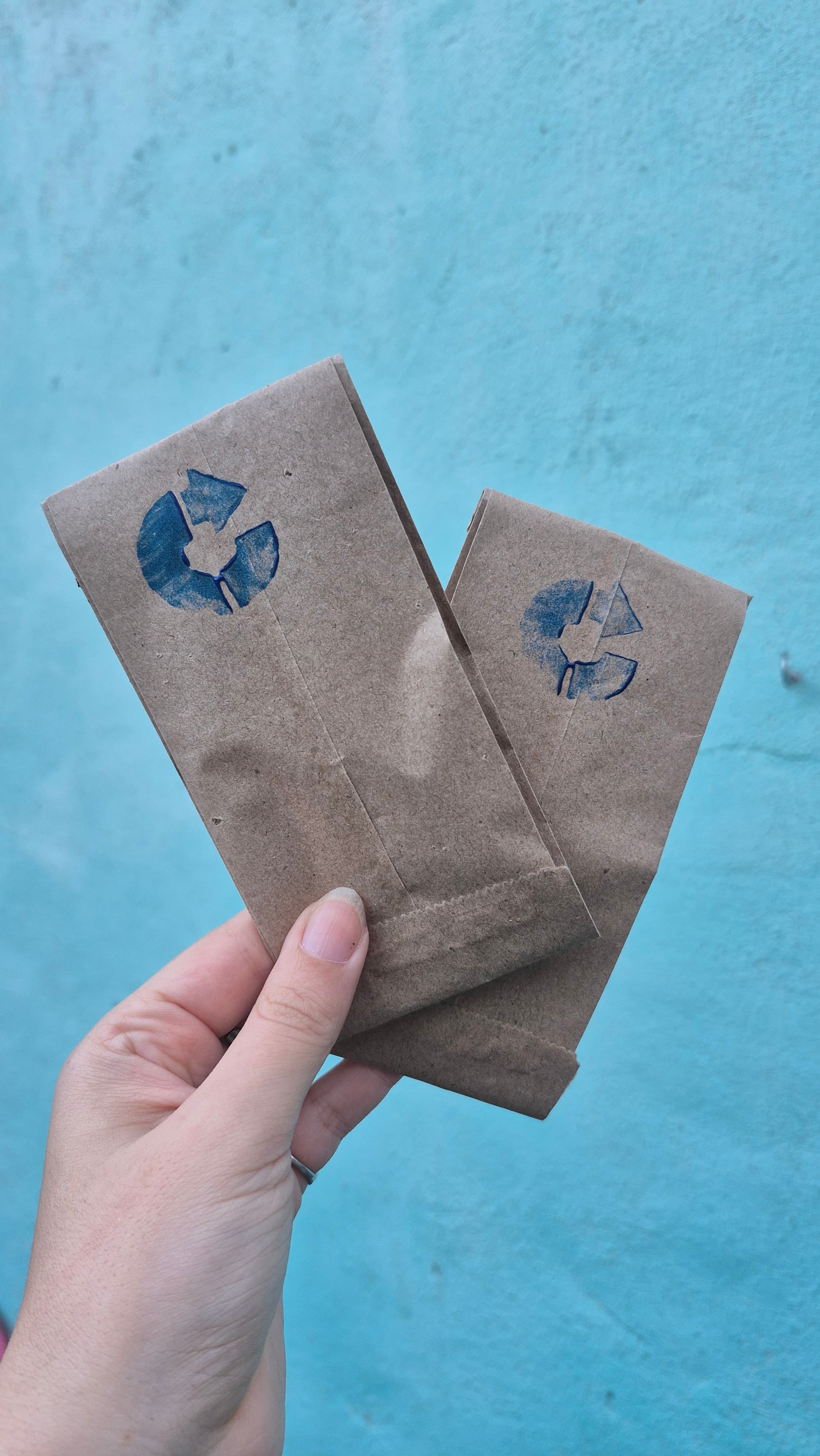 Una mano sostiene dos bolsitas de papel madera con el isotipo de CÍCLICA sellado en azul