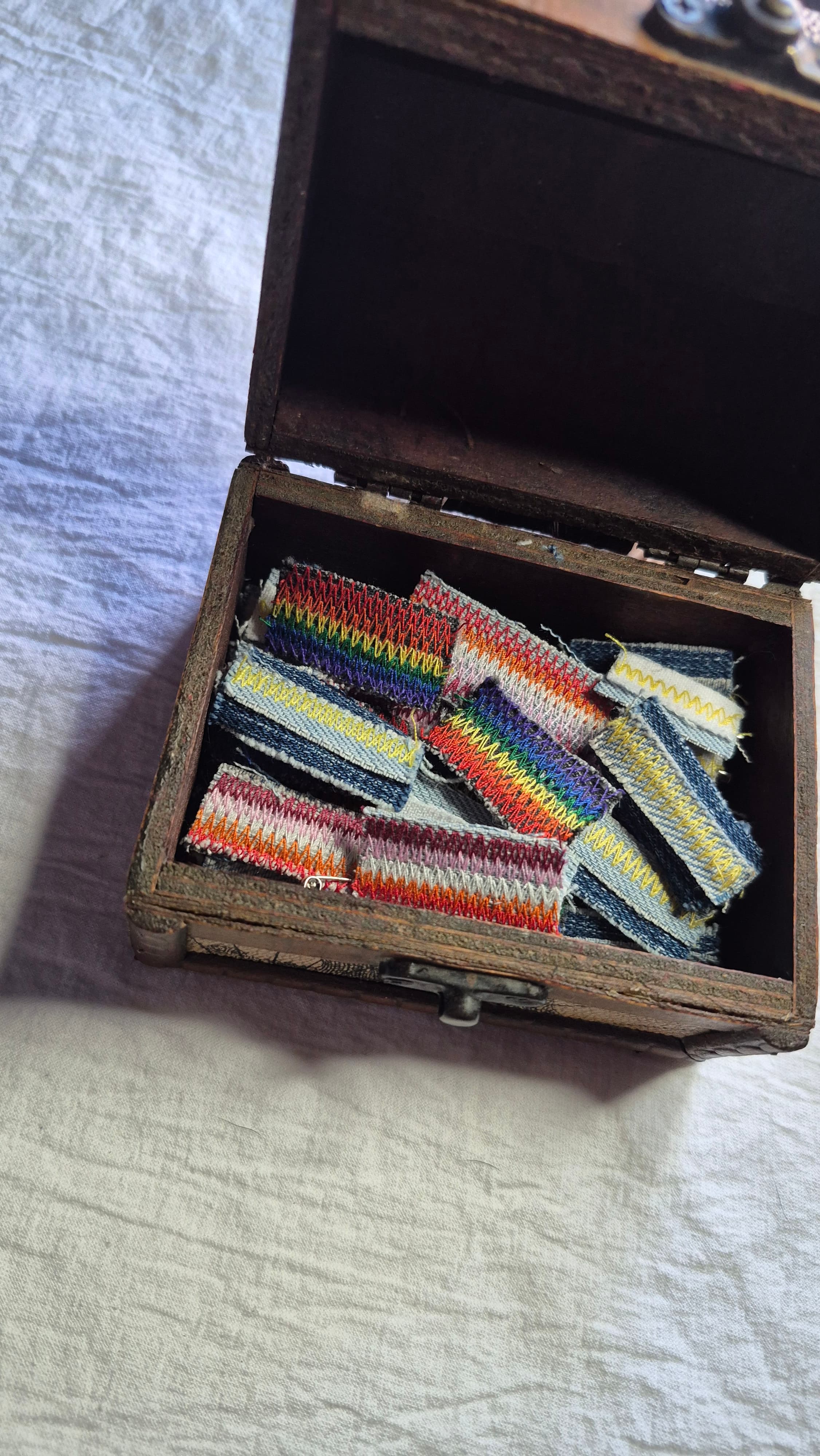 Un cofre de madera lleno de pins hechos con retazos de denim y bordados en zigzag de colores